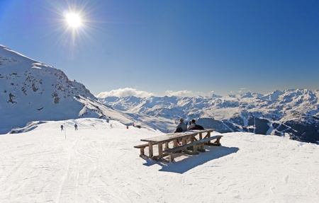Two skiers sat at picnic table relaxing on piste