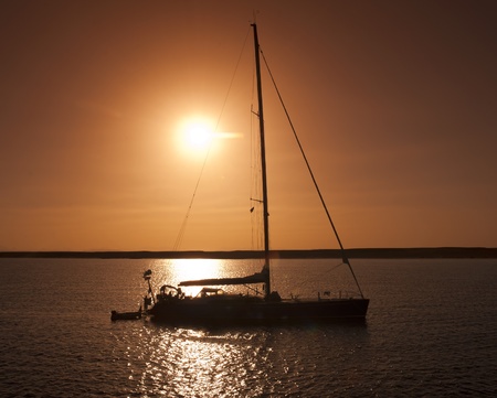 Private sailing yacht silhouetted at sunset whilst at anchorの写真素材