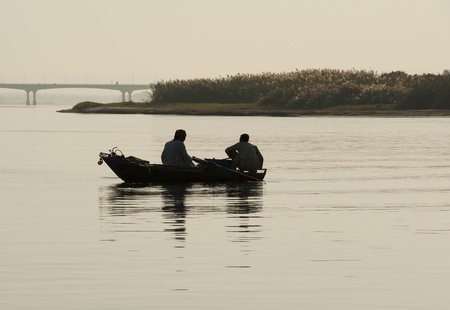 Traditional egyptian fishermen in a rowing boat silhouetted on the Nileの写真素材