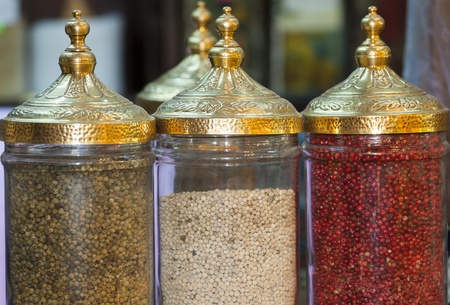 Display of peppercorns in ornate jars at an indoor market stall