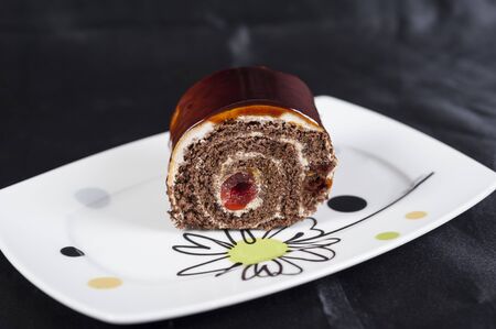 Chocolate sponge roll dessert with cherry on a white plateの写真素材