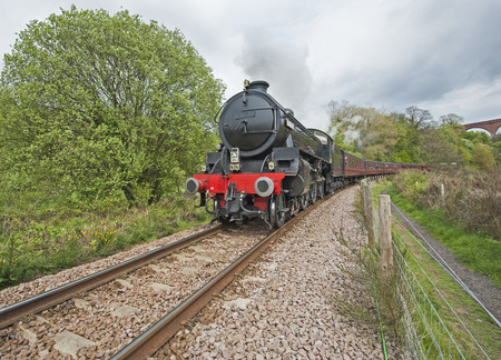Old english steam train travelling along tracks through rural countryside scenery