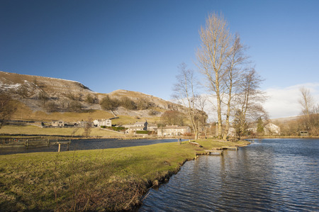 Bare trees during winter in english rural countryside landscape setting next to lake.
