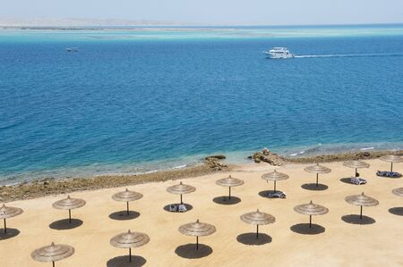 Aerial view over a tropical beach with rows of parasols and motor yacht sailingの写真素材