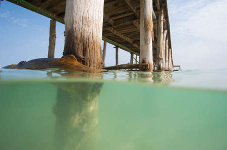 Long wooden jetty in the sea from a tropical island lagoon on beach showing underwater supportの写真素材