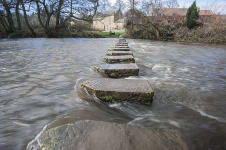Stepping stones across a small river in english rural village countryside scene.の写真素材
