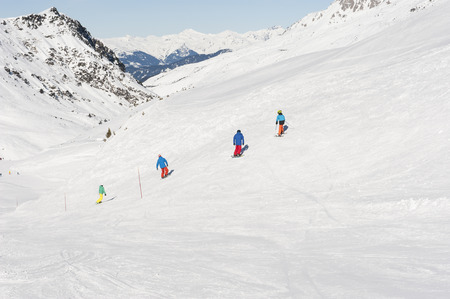 View down a snowy alpine piste with snowboarders and mountainsの写真素材
