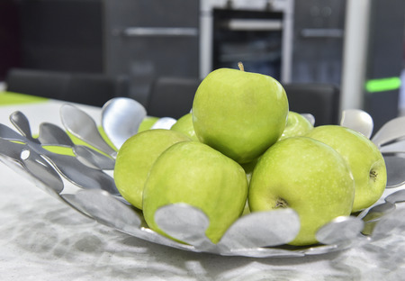 Collection of fresh green apples in a metal silver bowl on kitchen counter topの写真素材
