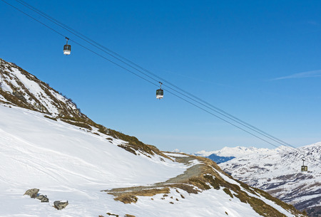 View of an alpine ski slope piste with cable car lift on mountain side
