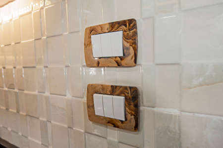 Closeup detail of two rocker light switch sockets on a white tiled kitchen wallの写真素材