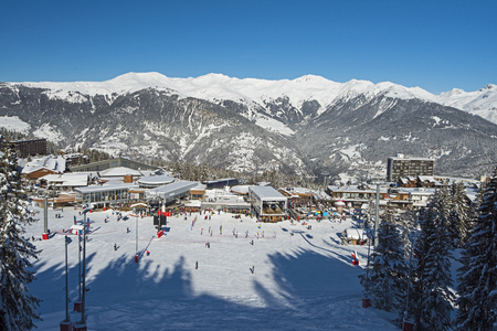 Panoramic view down snow covered valley in alpine mountain range with ski resort village center on blue sky backgroundの写真素材