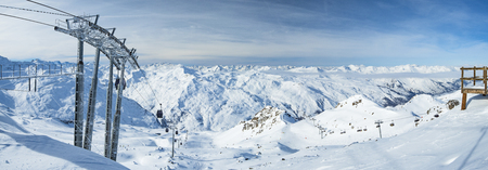 Panoramic view of a snow covered alpine mountain range with cable car ski lift over pisteの写真素材