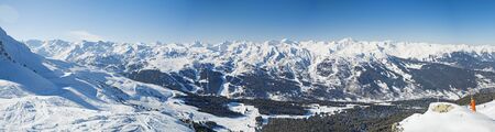 Panoramic view across snow covered alpine mountain range in alps on blue sky background