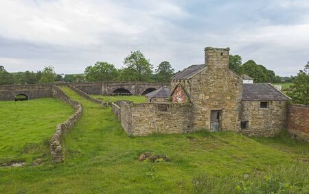 Old abandoned derelict mill stone building in rural countryside setting with overgrown bridge
