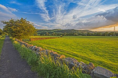Landscape view of rural countryside scenery with fields and meadows with cloudy sky