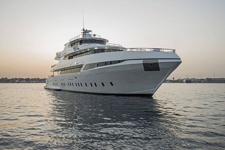 A luxury private motor yacht under way on tropical sea with bow wave at sunset