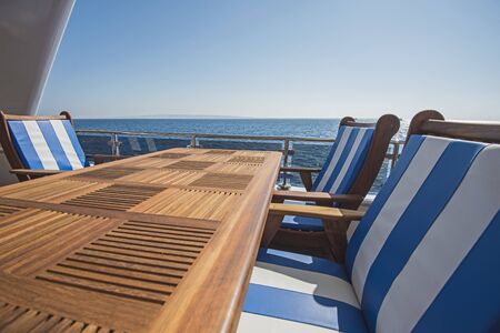 Sundeck of a large luxury motor yacht with chairs table and tropical sea view background