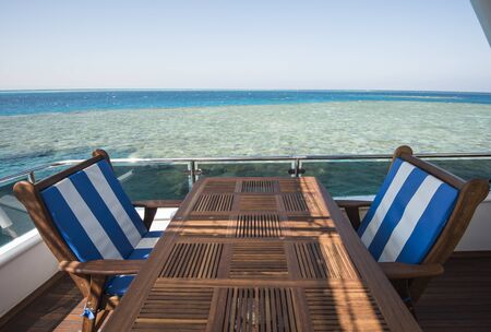 Sundeck of a large luxury motor yacht with chairs table and tropical sea view background