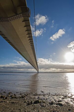 Large suspension bridge spanning a wide river estuary on a clear day with blue sky and cloudsの写真素材