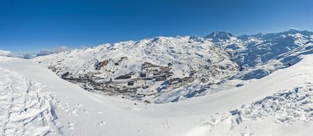 Panoramic view across snow covered alpine mountain range in alps on blue sky background with mountain villageの写真素材