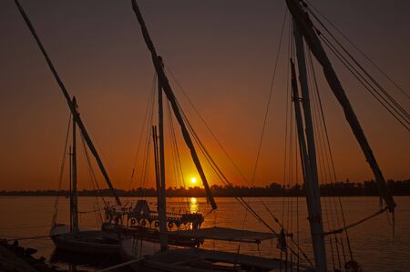 Traditional Egyptian felluca river boats moored on the Nile river bank with sunset and reflection in waterの写真素材