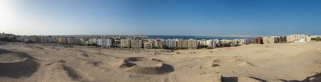 Panorama of large coastal town city with sea view on edge of arid harsh desert landscapeの写真素材