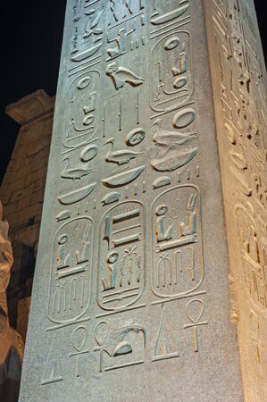 Large obelisk with hieroglyphic carvings at ancient egyptian Luxor Temple lit up during nightの写真素材