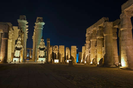 Large statues of Ramses II with columns in hypostyle hall at ancient egyptian Luxor Temple lit up during nightの写真素材