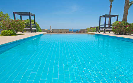 Large outdoor infinity swimming pool at a luxury tropical hotel resort with garden