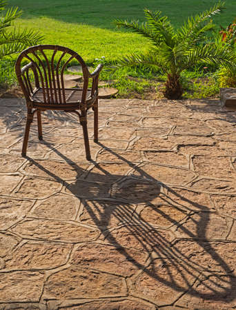 Abstract still life of wooden chair in outdoor in garden with long shadow cast over stone paving patio terraceの写真素材