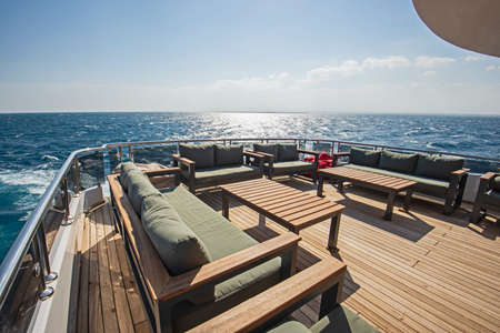 Teak stern wooden deck of a large luxury motor yacht with chairs sofa table and tropical sea view...