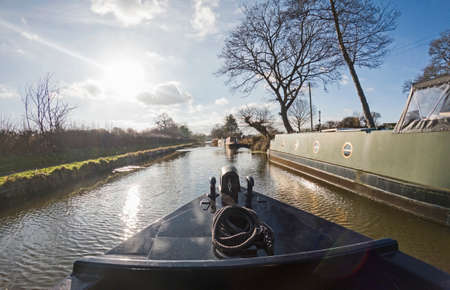 View from the bow of boat with narrowboats moored up in English rural countryside scenery on British tree lined waterway canalの素材 [FY310181629293]