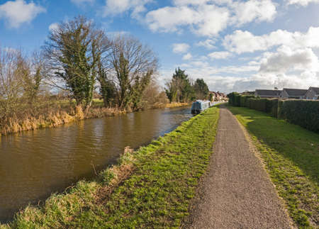 Narrowboat moored up in English rural countryside scenery on British waterway canal with cloudy blue skyの写真素材