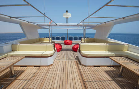 Teak wooden sundeck of a large luxury motor yacht with chairs sofa table and tropical sea view...