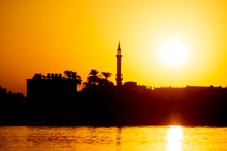 View across large wide river Nile in Egypt through rural countryside landscape with beautiful orange sunset and mosque minaret architectureの写真素材