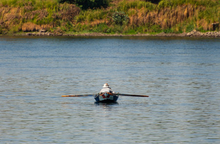 Traditional fisherman in rowing boat on river fishing by riverbank