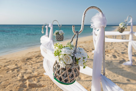 Closeup detail setup of wedding day marriage aisle with drapes and hanging basket flowers on sandy tropical beach paradise to open ocean backgroundの写真素材
