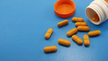 Orange medical pills and tablets spilling out of a drug bottle. Macro top down view with copy space. Pills on light blue background. side viewの写真素材