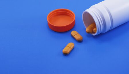 Orange medical pills and tablets spilling out of a drug bottle. Macro top down view with copy space. Pills on dark blue background.の写真素材