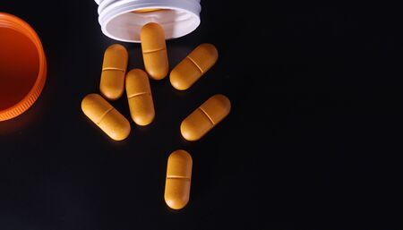 Orange medical pills and tablets spilling out of a drug bottle. Macro top down view with copy space. Pills on black background. the view from the topの写真素材