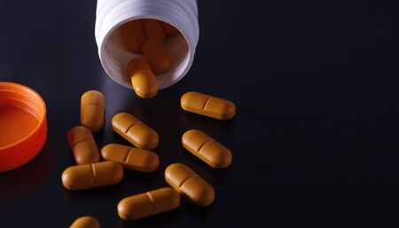 Orange medical pills and tablets spilling out of a drug bottle. Macro top down view with copy space. Pills on black background.の写真素材