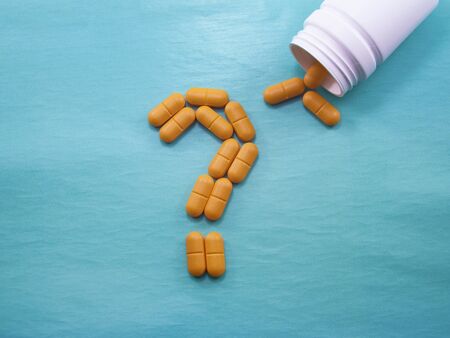 A lot of orange pills scattered on a blue background. A question mark laid out of pills. Counterfeit medicinal products. Empty space to insert textの写真素材