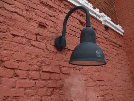 A black metal round lantern on a brick red exterior wall in the grounds of an old ruined factoryの写真素材