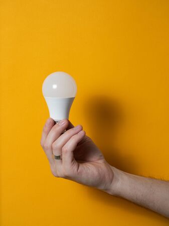 The hand of a man holding a light bulb for innovation and creative concept. Light bulb in hand on a yellow background. Empty space for your textの写真素材