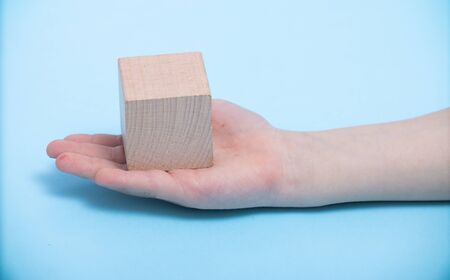 close-up of a hand placing wooden block on a blue background. A child's hand holds a cube. Space for your textの写真素材