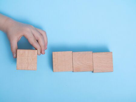 close-up of a hand placing wooden block on a blue background. A child's hand holds a cube. Space for your textの写真素材