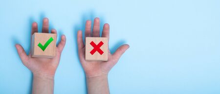 close-up of a hands placing two wooden blocks on a blue background. True and false symbols accept rejected for evaluation, Yes or No on wood blocks on blue background.の写真素材