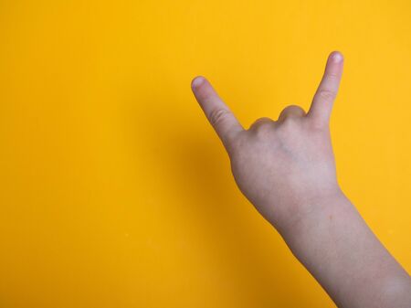 a child making a rock gesture isolated on a yellow background. A beautiful young teen shows her horns up with a gesture.の写真素材