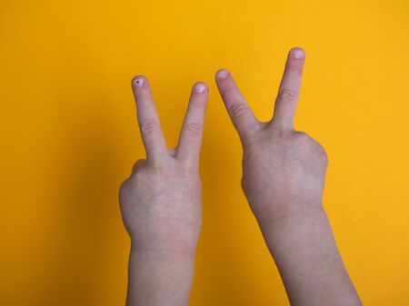 isolated child hand shows the number two on yellow backgroundの写真素材