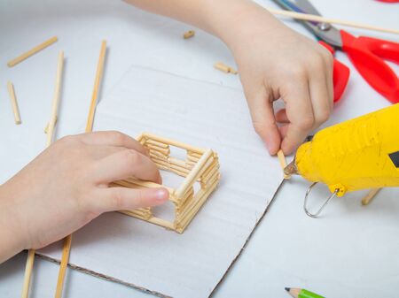 step-by-step instructions for creating a house from bamboo sticks. children's creativity, manual work, online classes. step 5. using a glue gun, the child attaches bamboo sticksの写真素材
